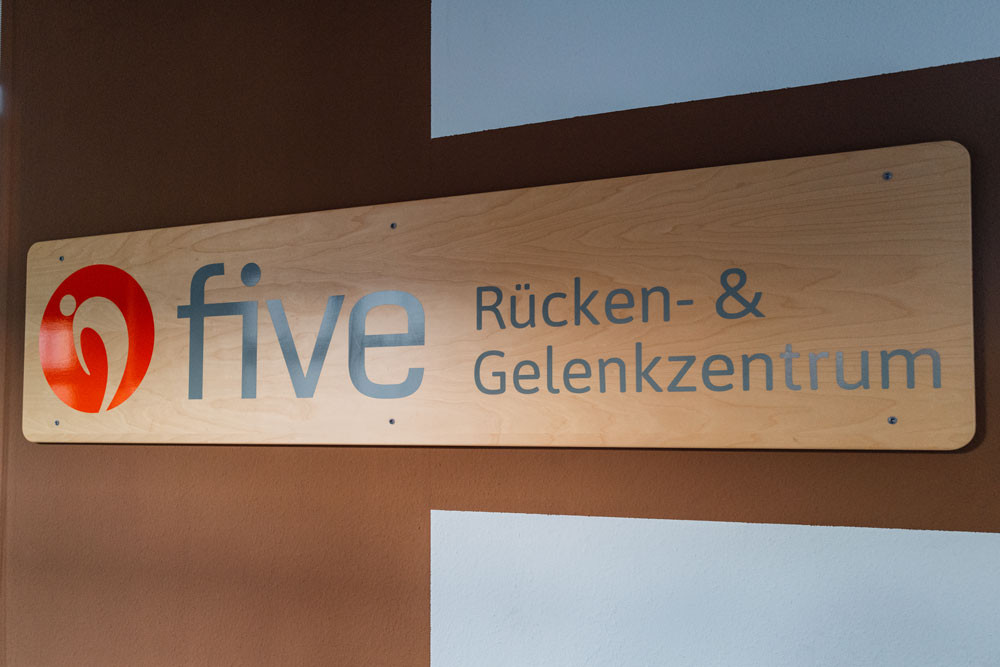 Auf einem Schild aus Holz an der Wand steht five Rücken- & Gelenkzentrum.